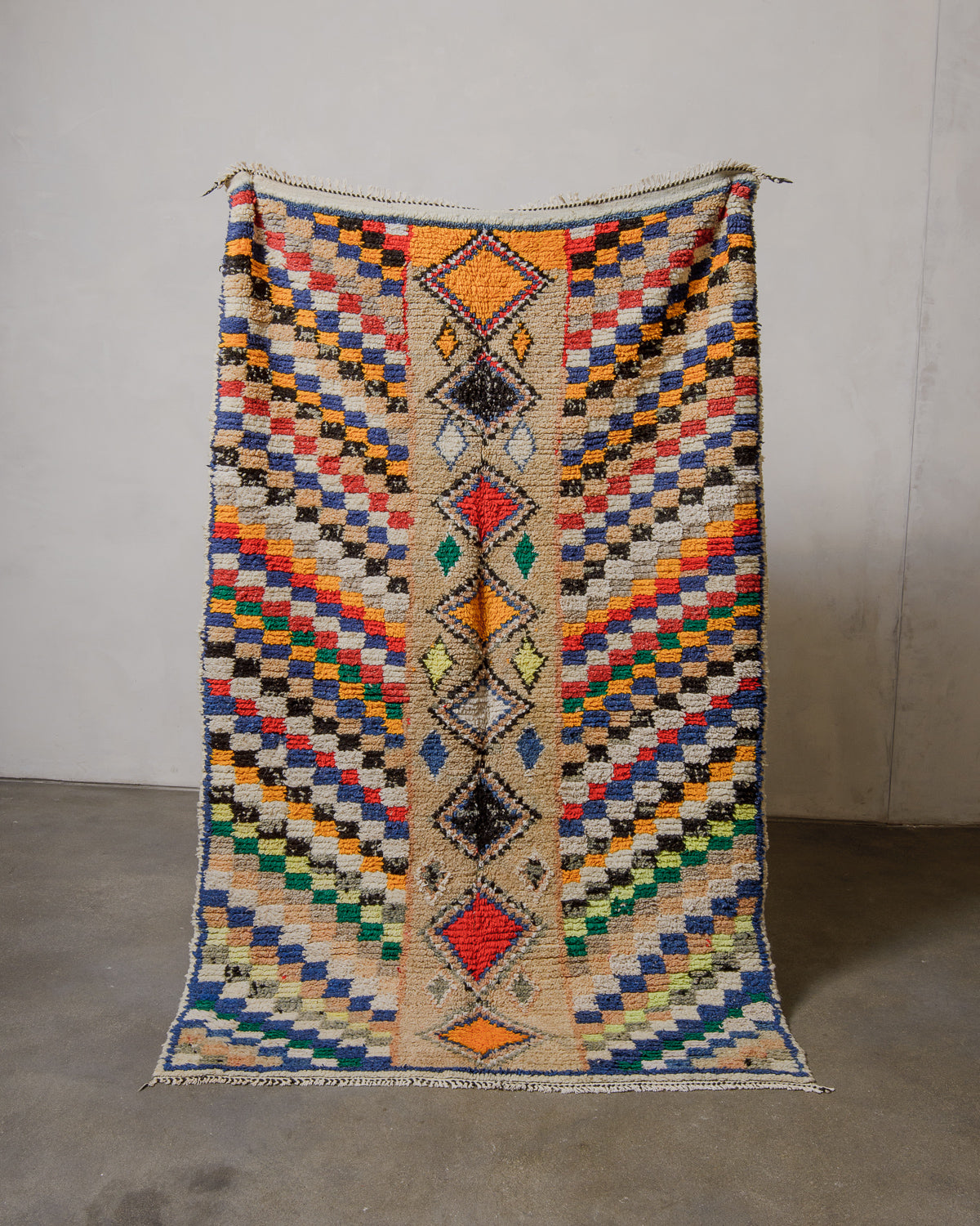 Vintage wool rug with geometric design held in front of a plain wall.
